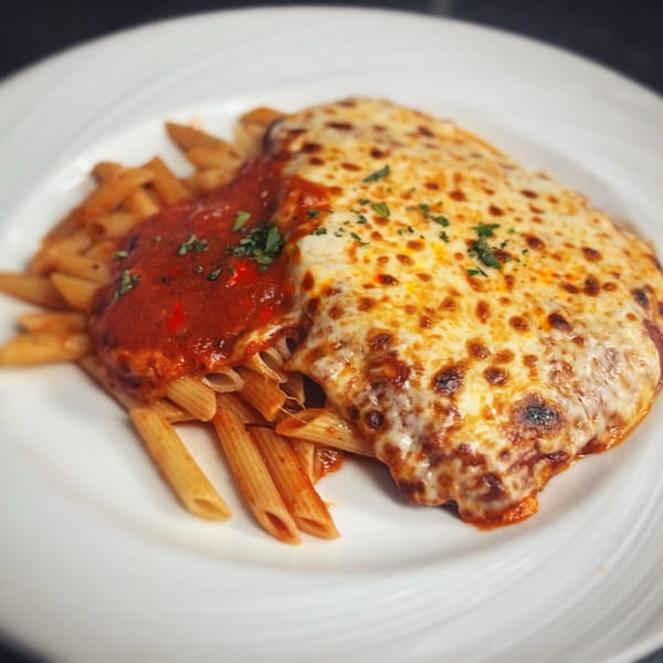 Chicken Parmesan with penne pasta and marinara sauce, topped with melted cheese and parsley.