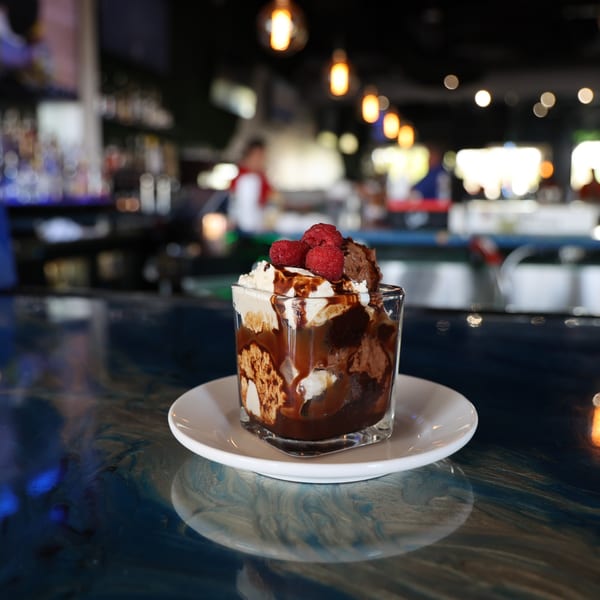 Chocolate and vanilla dessert with raspberries and chocolate drizzle on a bar counter.