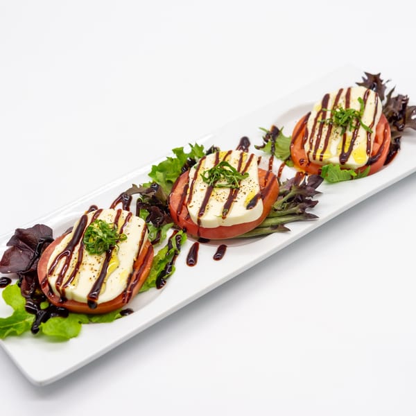 Three Caprese salad stacks with tomato, mozzarella, basil, balsamic glaze, and olive oil.