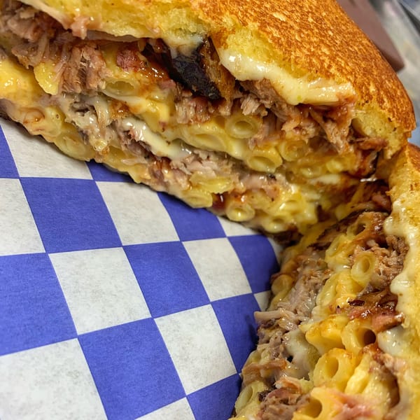 Close-up of a grilled cheese sandwich filled with pulled pork and macaroni and cheese on checkered paper.