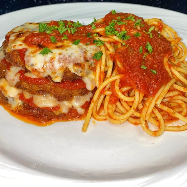 Chicken Parmesan with melted cheese and red sauce, served alongside spaghetti on a white plate.