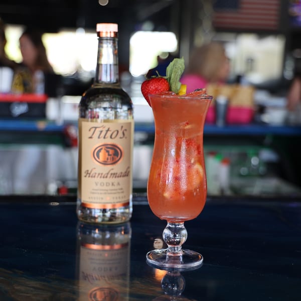 Tito's Handmade Vodka bottle next to a strawberry cocktail garnished with mint and fruit.