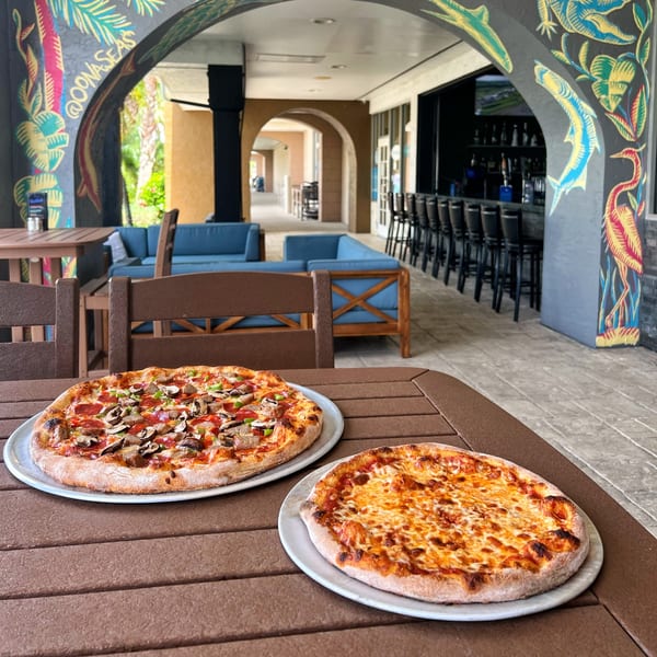 Two pizzas, one cheese and one with toppings, on a table at The Hangout by Two Guys.