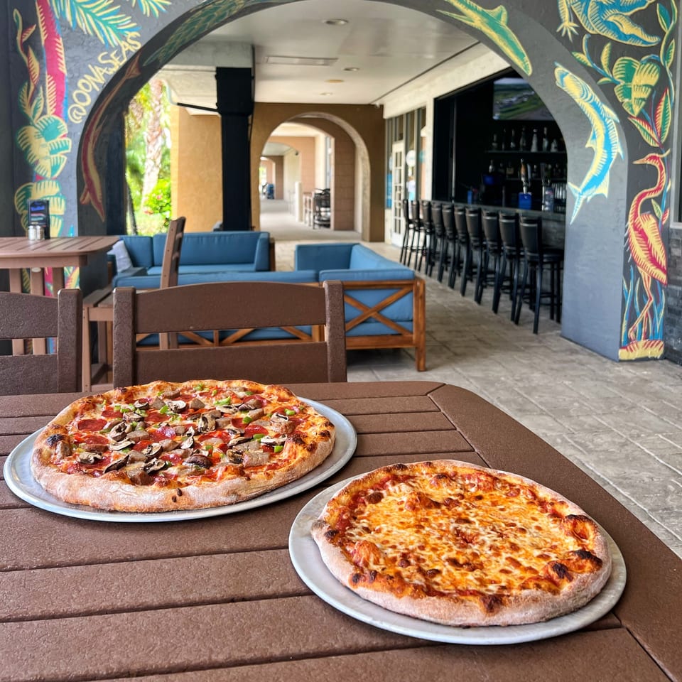 Two pizzas, one cheese and one with toppings, on a table at The Hangout by Two Guys.