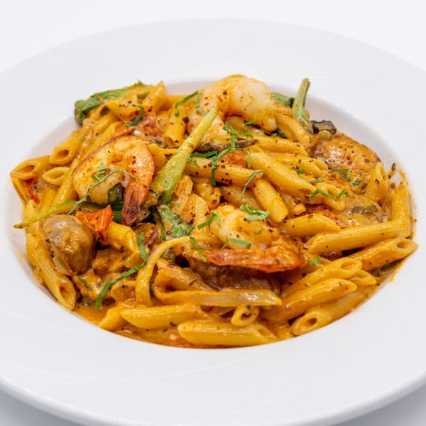 Penne pasta with shrimp, mushrooms, tomatoes, and green beans in a creamy orange sauce.