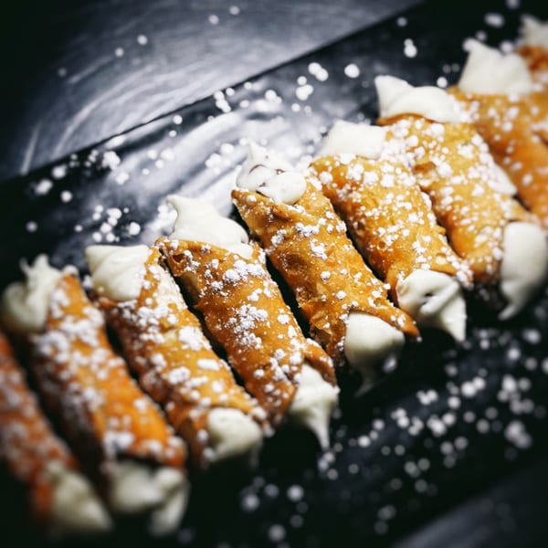 A row of golden-brown cannoli filled with white cream and dusted with powdered sugar.