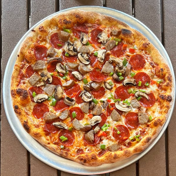 A whole pepperoni, sausage, mushroom, and bell pepper pizza on a metal tray.