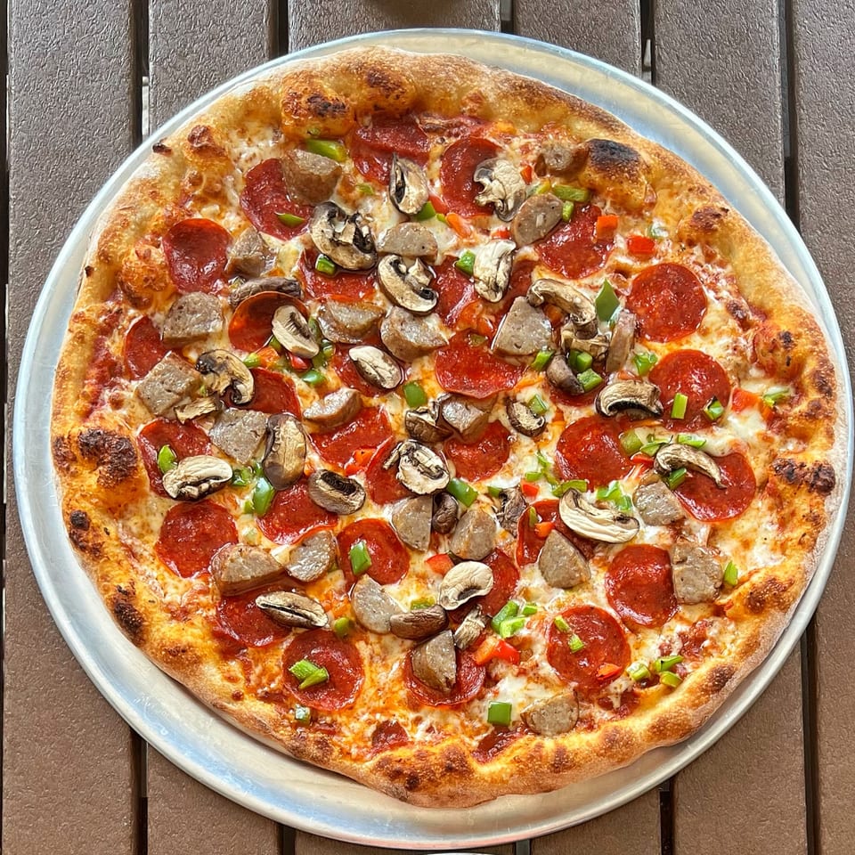 A whole pepperoni, sausage, mushroom, and bell pepper pizza on a metal tray.