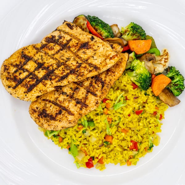 Grilled chicken breasts with yellow rice and mixed vegetables, including broccoli, carrots, and mushrooms.