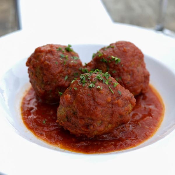 Three Italian meatballs covered in red sauce and parsley, served in a white bowl.